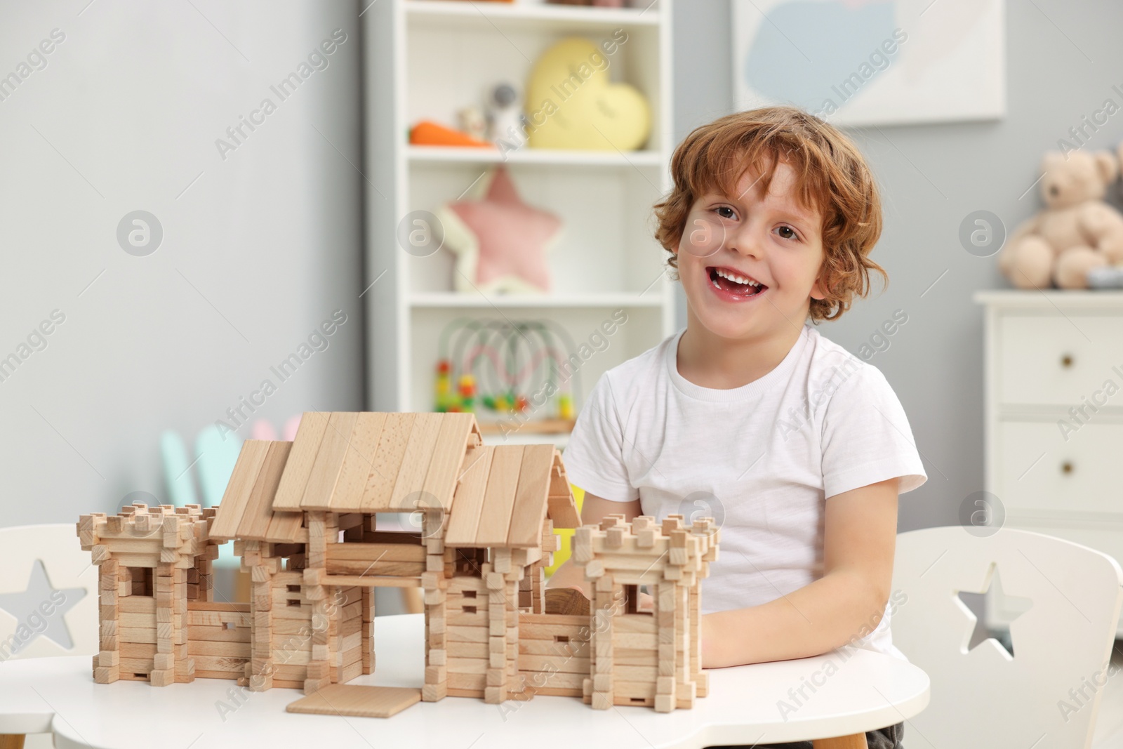 Photo of Little boy playing with wooden entry gate at white table in room. Child's toy