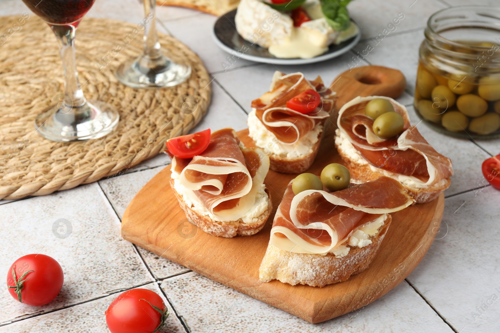 Photo of Tasty sandwiches with cured ham, tomatoes and olives on tiled table