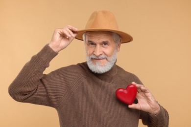 Senior man in hat with red decorative heart on beige background