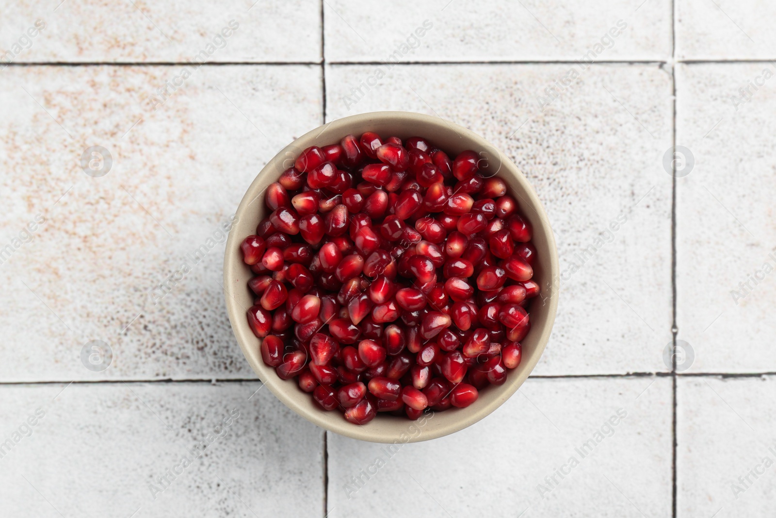 Photo of Tasty ripe pomegranate grains on tiled table, top view