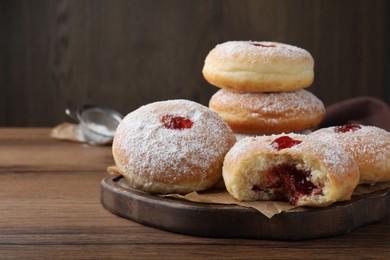 Photo of Delicious donuts with jelly and powdered sugar on wooden table