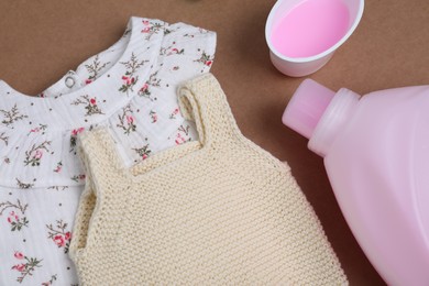 Photo of Laundry detergents and baby clothes on brown background, flat lay