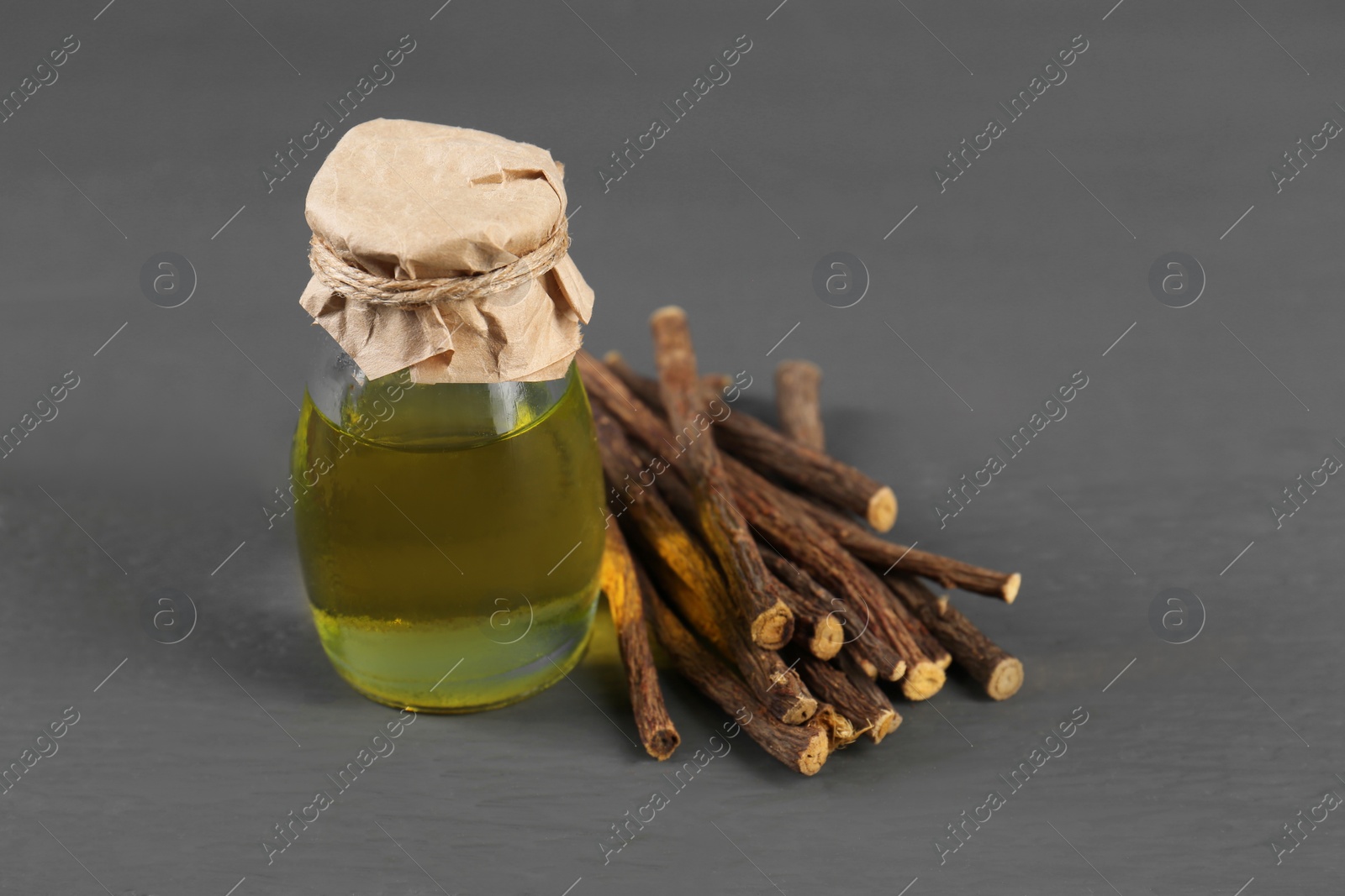 Photo of Dried sticks of licorice roots and essential oil on grey wooden table