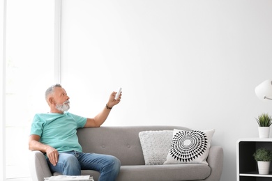 Photo of Senior man with air conditioner remote control at home
