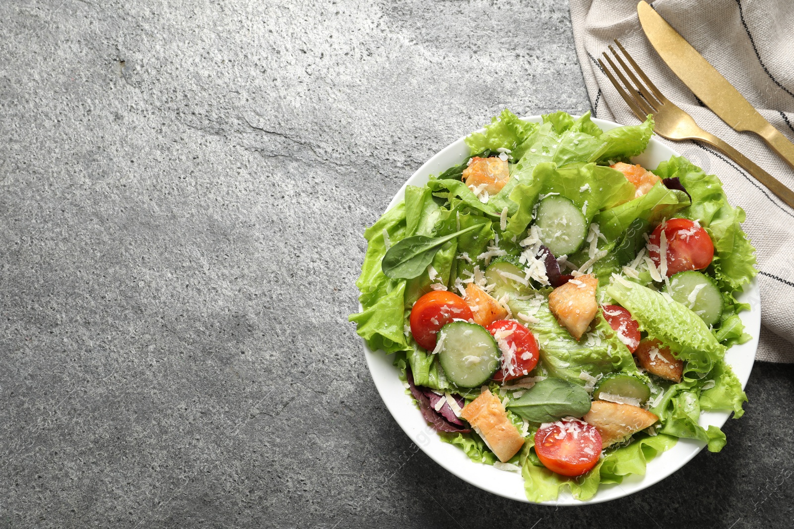 Photo of Delicious salad with chicken, cheese and vegetables served on grey table, top view. Space for text