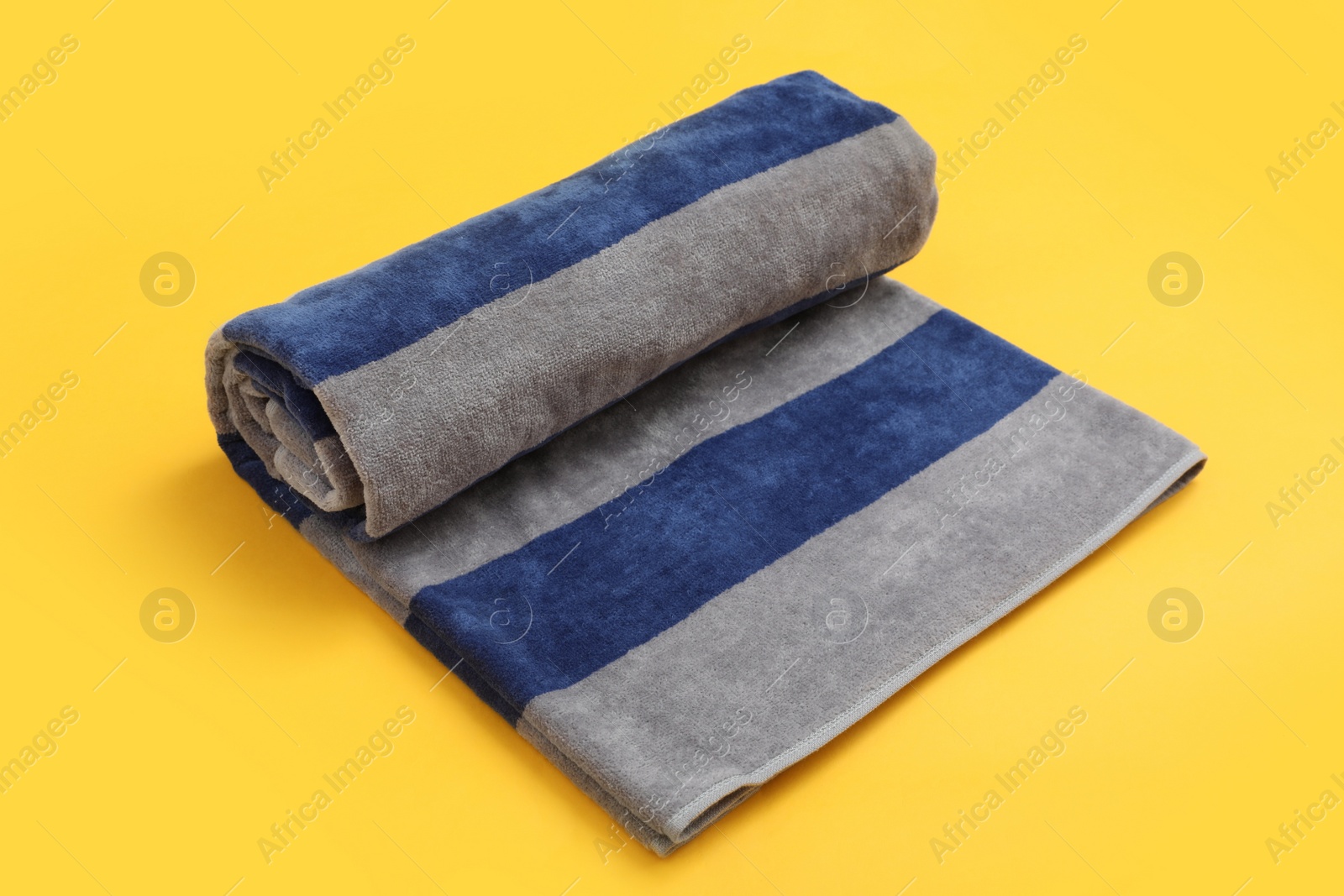 Photo of Rolled striped beach towel on yellow background