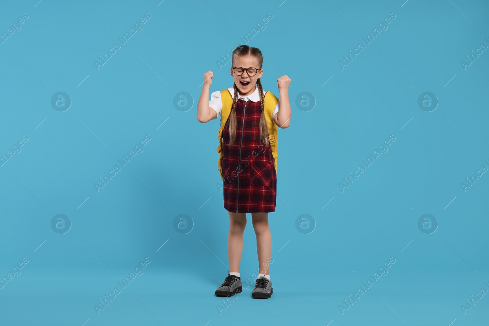 Photo of Emotional schoolgirl in glasses with backpack on light blue background