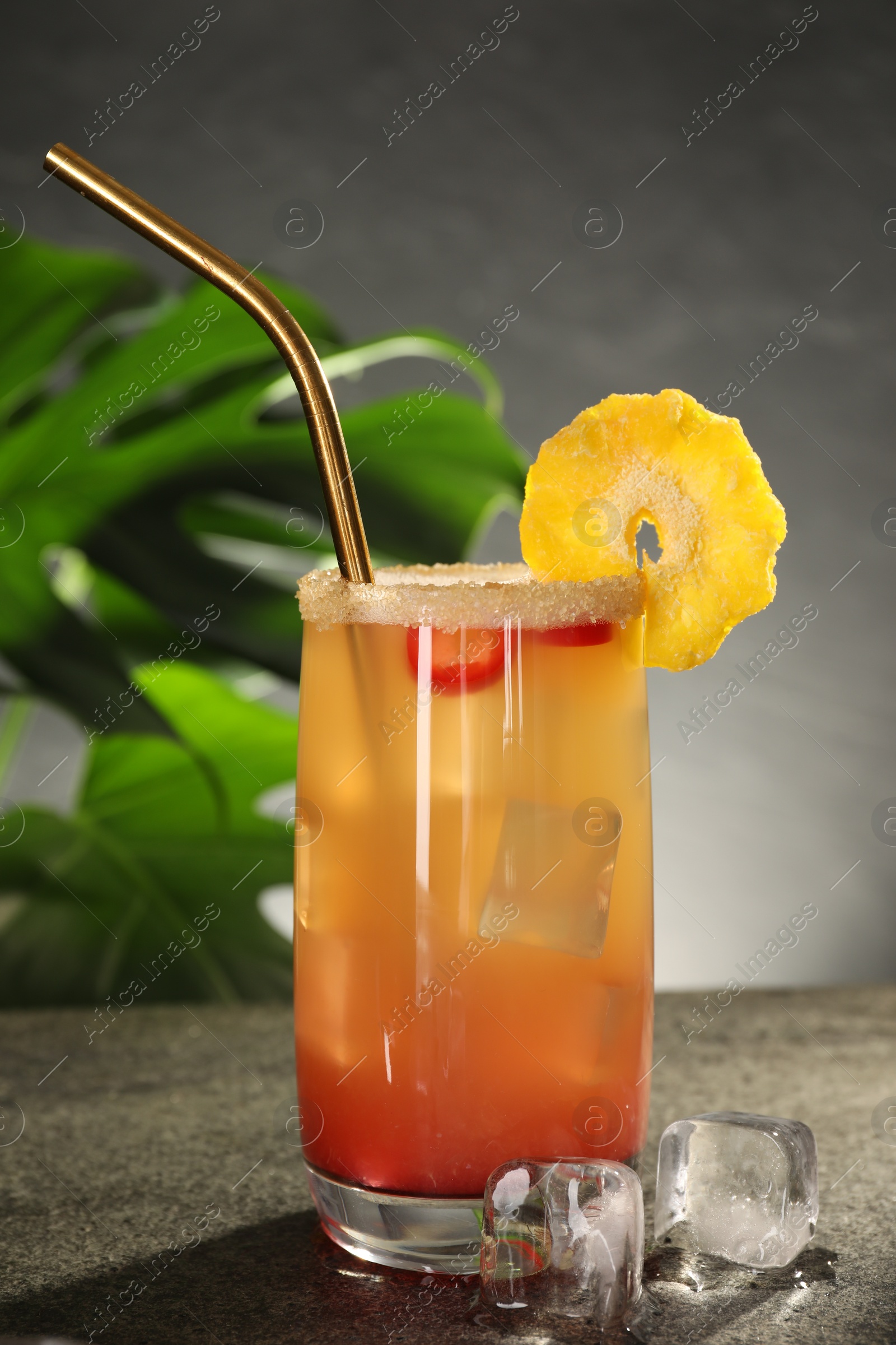 Photo of Glass of tasty pineapple cocktail and ice cubes on grey table