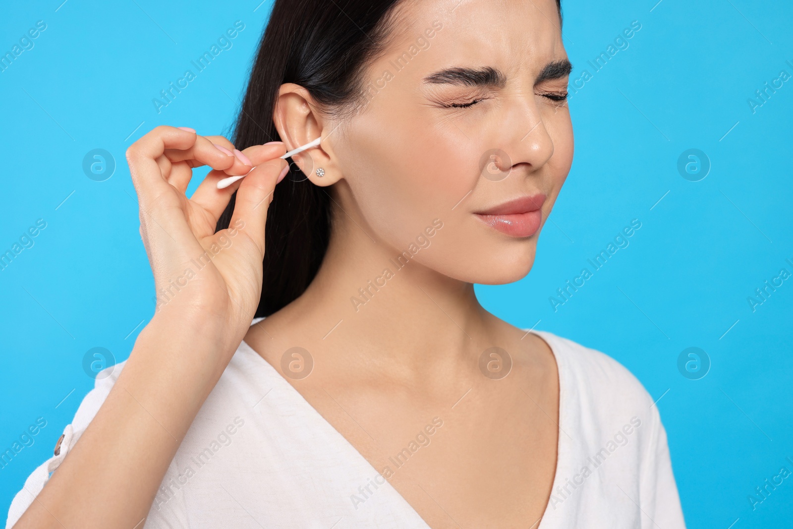 Photo of Young woman cleaning ear with cotton swab on light blue background, closeup