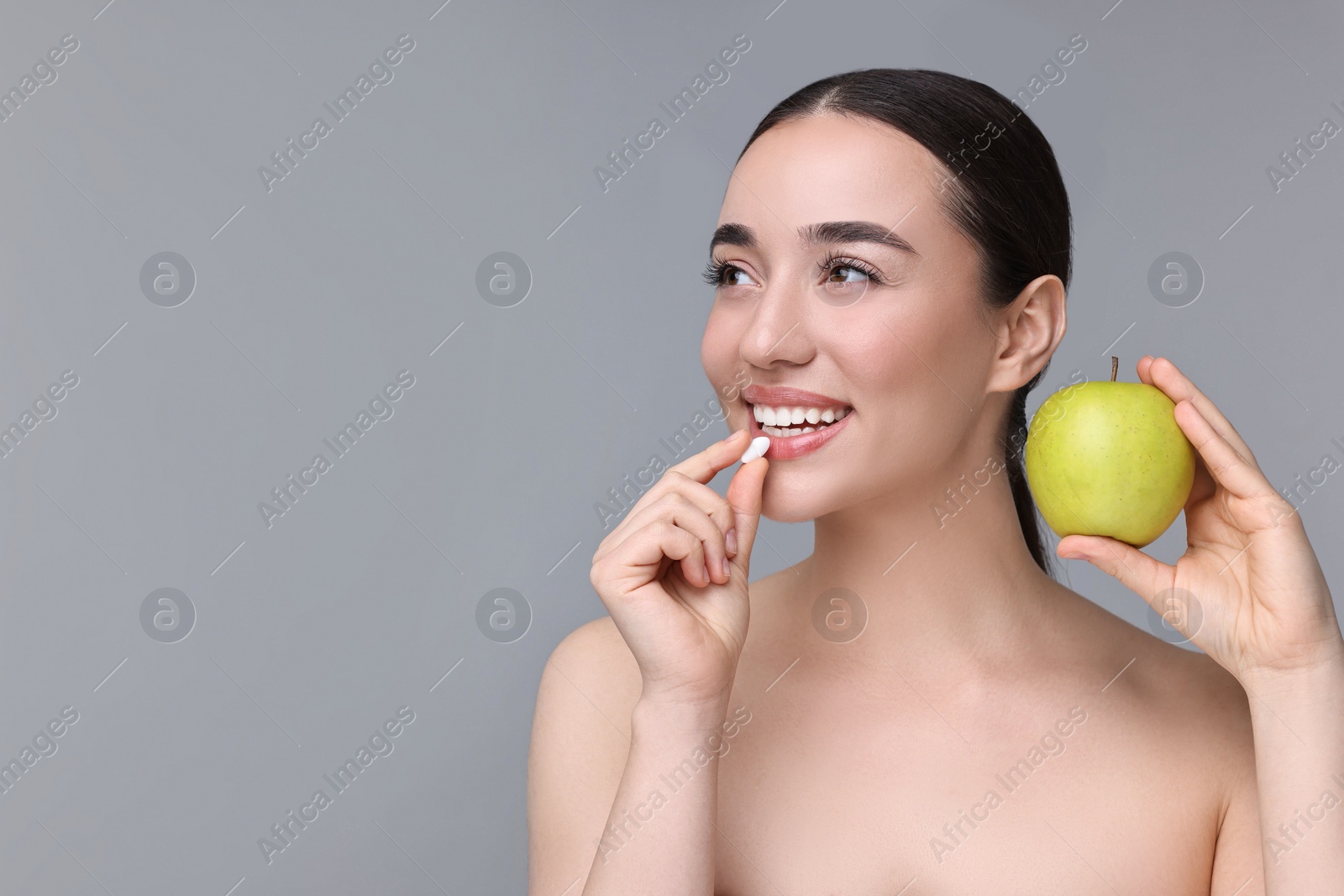 Photo of Beautiful young woman with vitamin pill and apple on grey background. Space for text