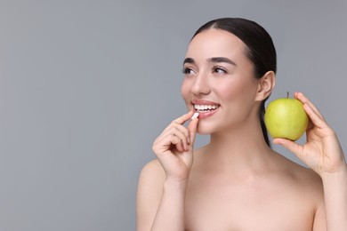 Photo of Beautiful young woman with vitamin pill and apple on grey background. Space for text