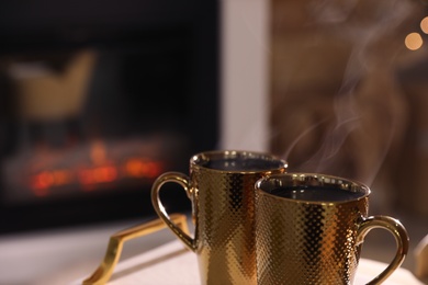 Photo of Golden cups with hot drinks against fireplace, closeup. Space for text