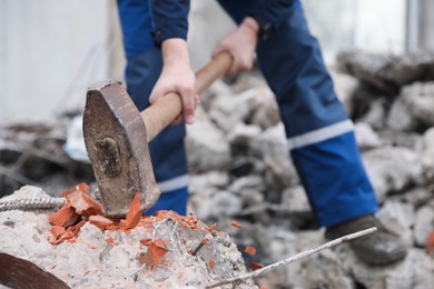 Photo of Man breaking brick with sledgehammer outdoors, selective focus