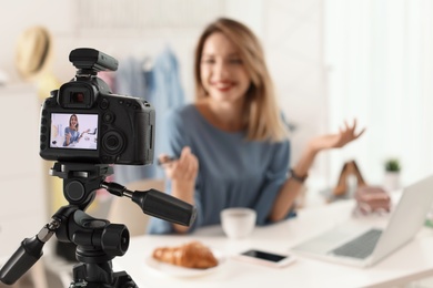 Photo of Fashion blogger recording video indoors, focus on camera display. Space for text
