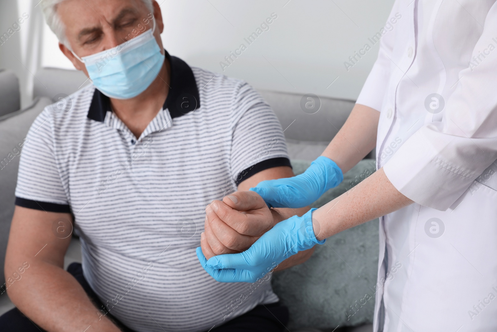 Photo of Doctor checking pulse of senior man with protective mask at nursing home, closeup