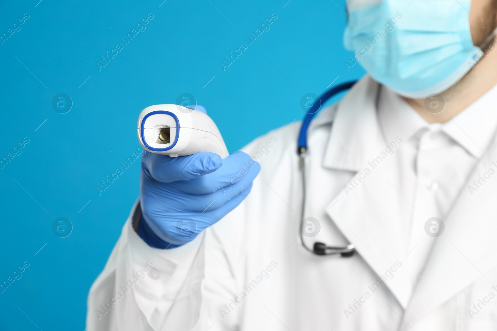 Photo of Doctor holding non contact infrared thermometer against light blue background, focus on hand. Measuring temperature