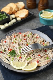 Photo of Tasty pickled anchovies with spices and fork on grey table