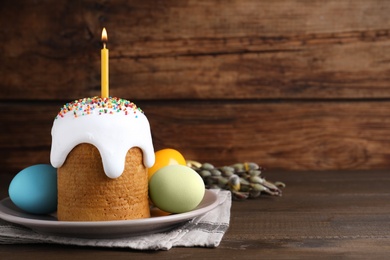 Traditional Easter cake with burning candle and colorful eggs on wooden table. Space for text