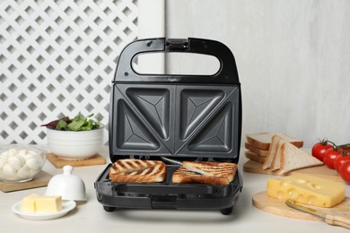 Photo of Modern grill maker with sandwiches and different products on white table