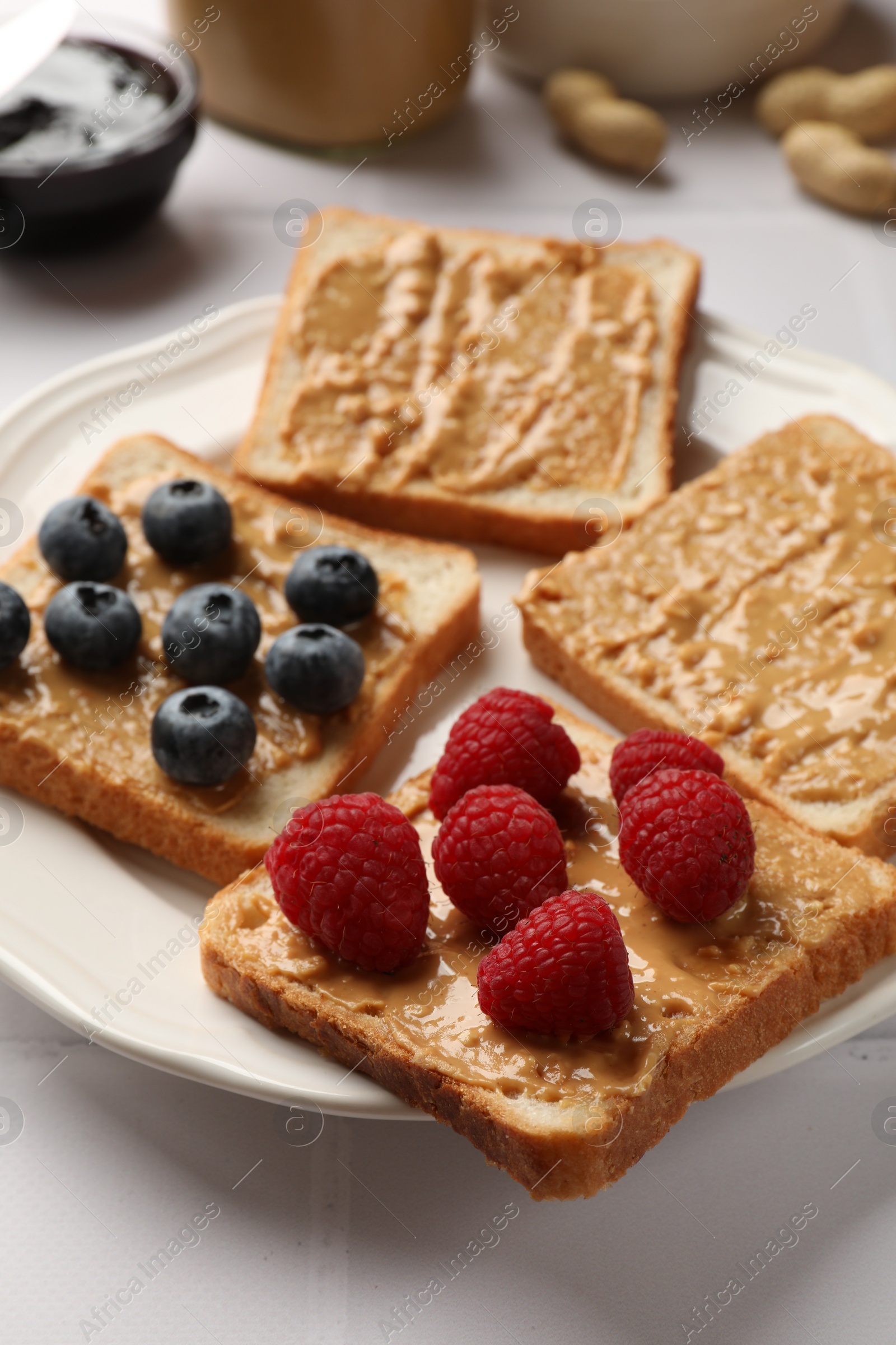 Photo of Delicious toasts with peanut butter, raspberries and blueberries on white table