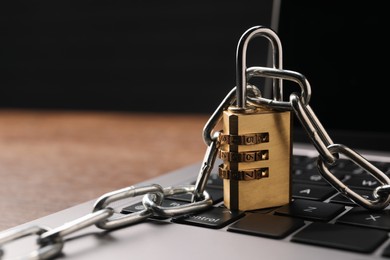 Photo of Cyber security. Laptop with padlock and chain on table, closeup