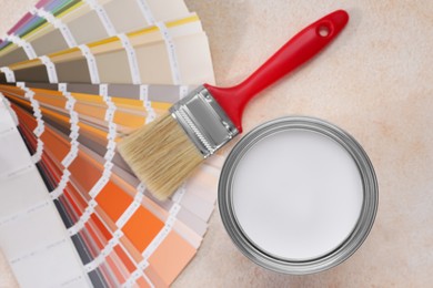 Photo of Can of white paint, brush and palette on beige table, flat lay