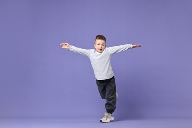 Photo of Happy little boy dancing on violet background