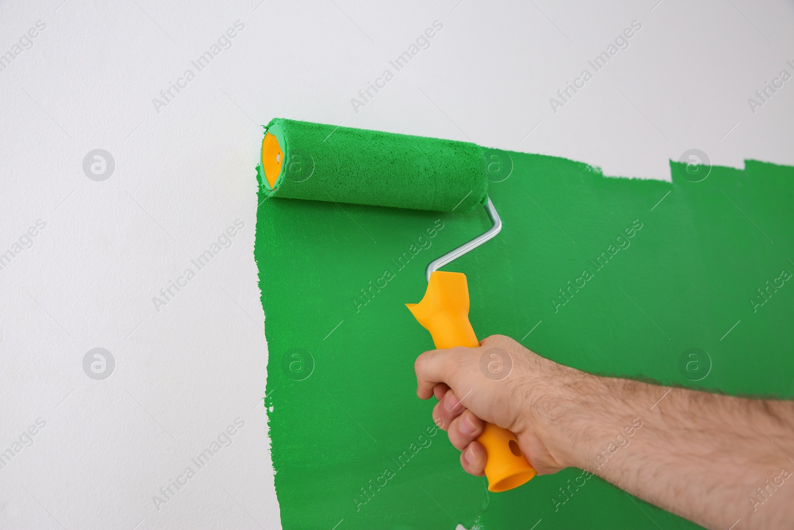 Photo of Man painting white wall with green dye, closeup. Interior renovation