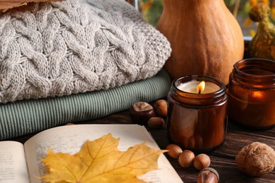 Burning scented candles, warm sweaters, book and pumpkins on wooden table. Autumn coziness
