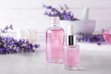 Photo of Bottles of essential oil and lavender flowers on white wooden table