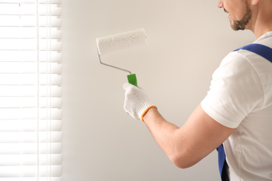 Photo of Man painting wall with white dye indoors, closeup