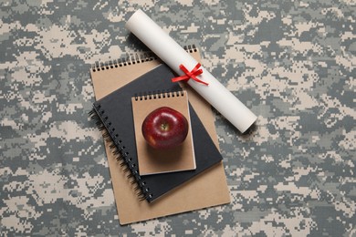 Photo of Notebooks, apple and diploma on camouflage background, flat lay. Military education