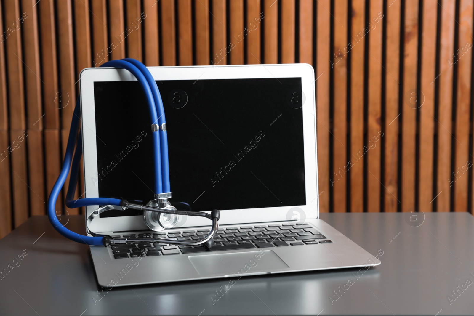 Photo of Laptop with blank screen and stethoscope on table against wooden background, space for text. Computer repair