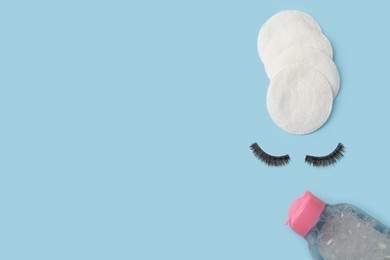 Photo of Bottle of makeup remover, cotton pads and false eyelashes on light blue background, flat lay. Space for text