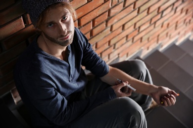 Photo of Male drug addict making injection on stairs near brick wall