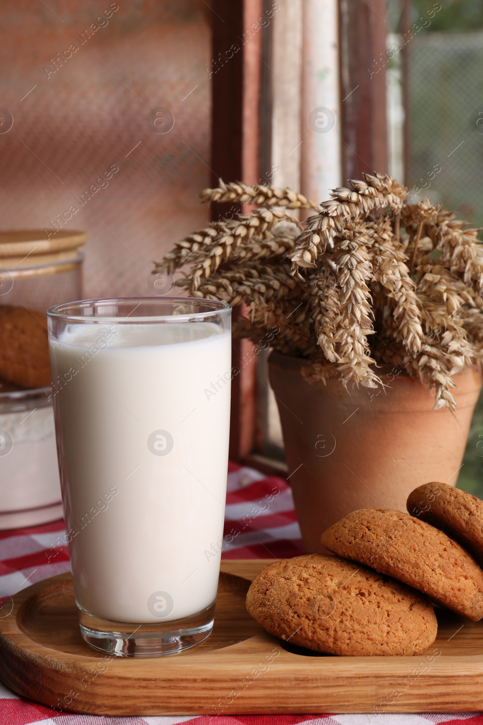 Photo of Glass of milk with cookies on red checkered tablecloth indoors