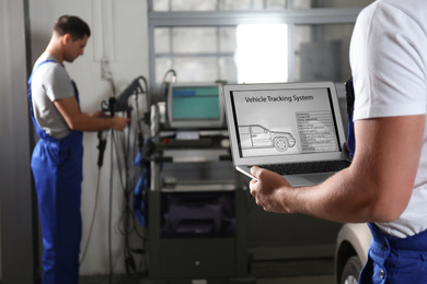 Photo of Mechanic with laptop doing car diagnostic at automobile repair shop, closeup. Space for text