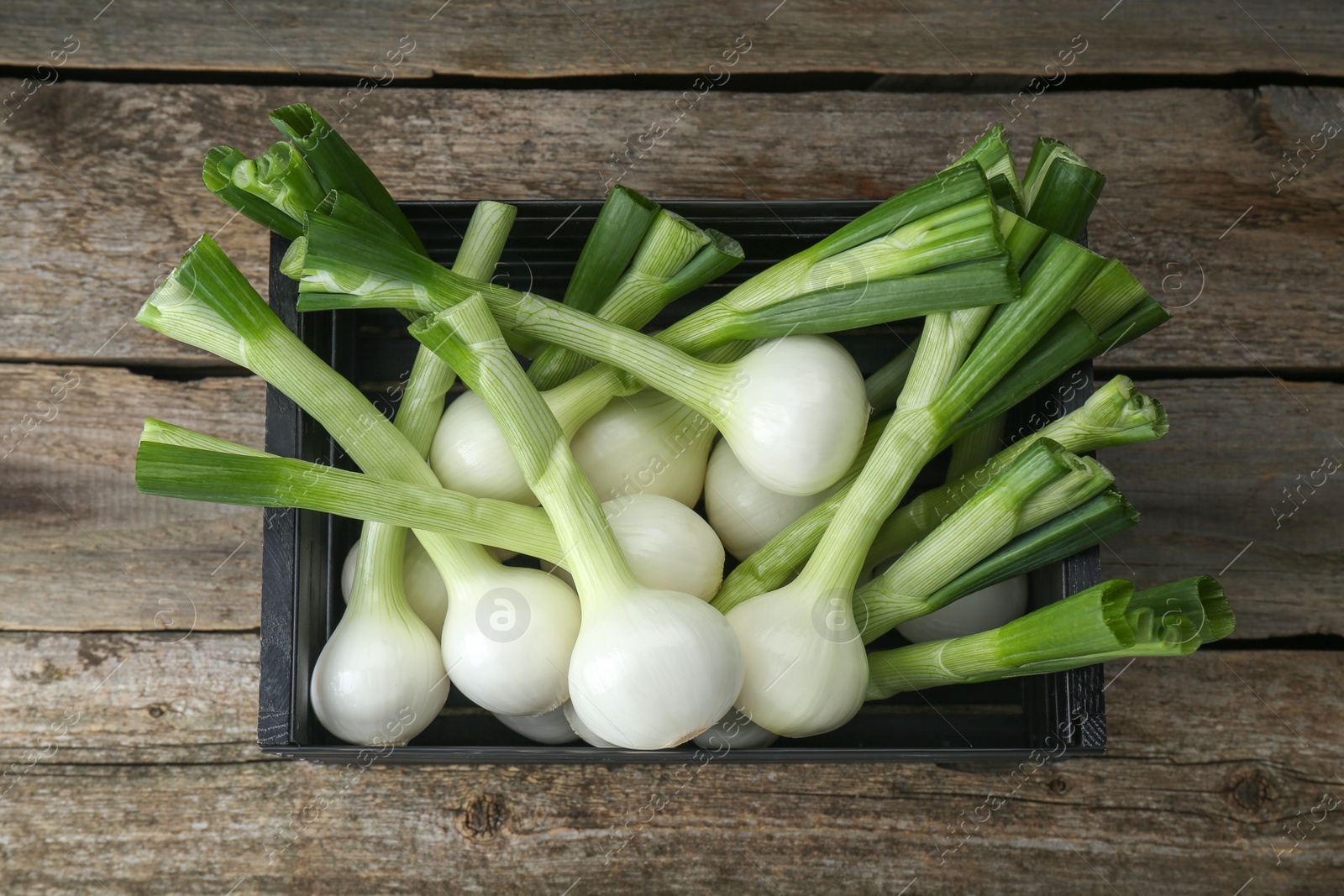 Photo of Black crate with green spring onions on wooden table, top view