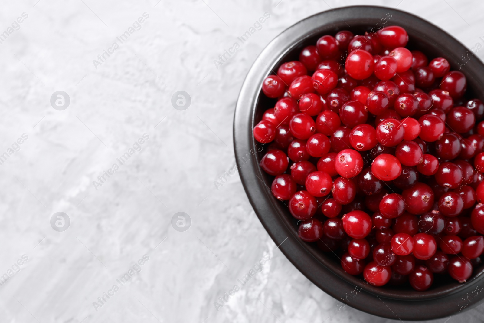 Photo of Fresh ripe cranberries in bowl on grey table, top view. Space for text