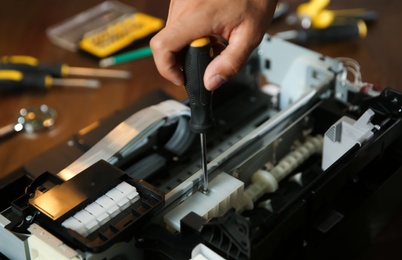 Photo of Repairman with screwdriver fixing modern printer, closeup