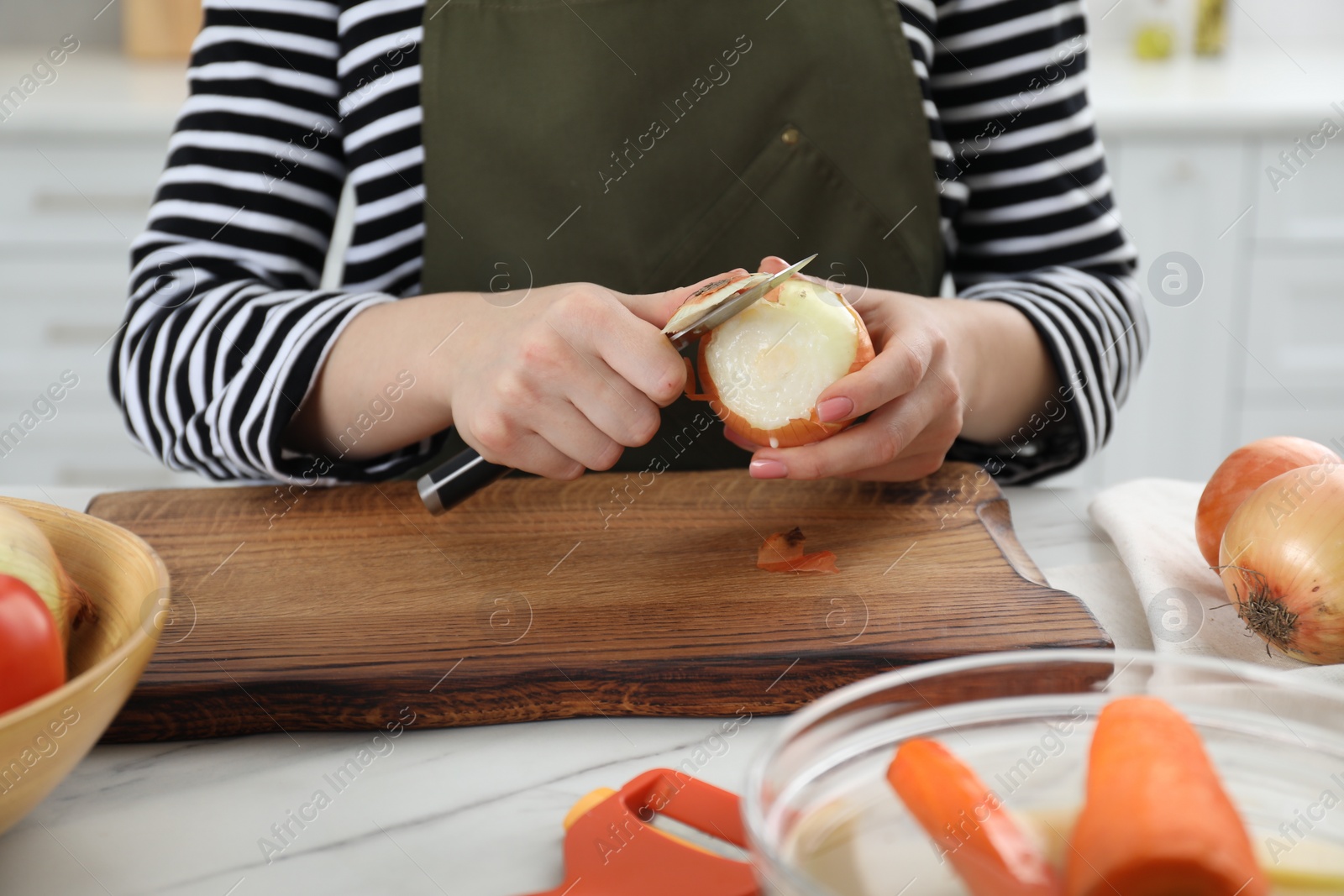 Photo of Woman peeling fresh onion with knife at white marble table indoors, closeup