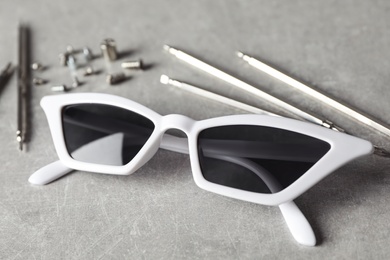 Stylish female sunglasses and fixing tools on grey table