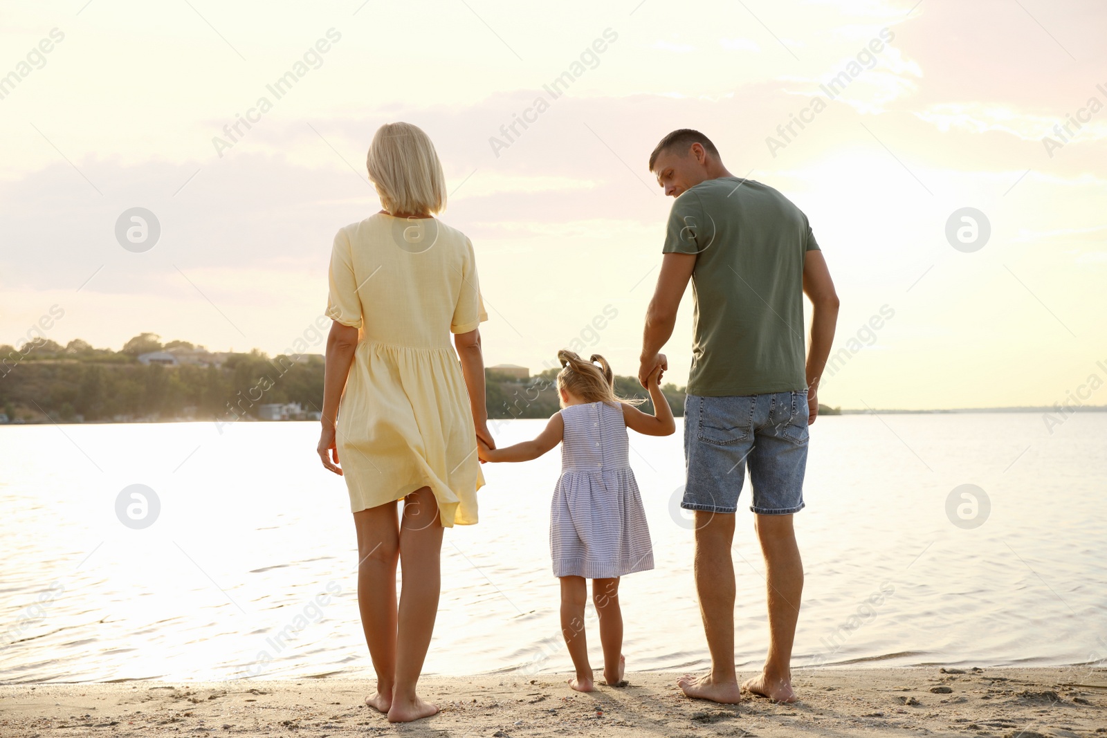 Photo of Happy parents with their child on beach, back view. Spending time in nature