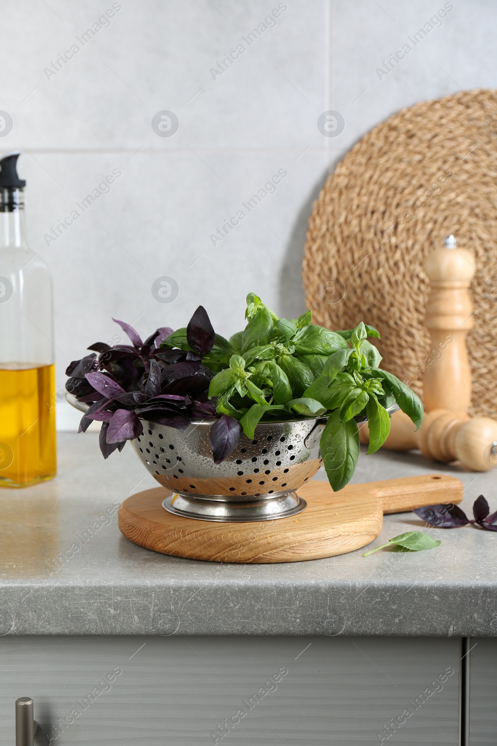 Photo of Metal colander with different fresh basil leaves on grey countertop in kitchen