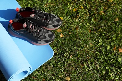 Photo of Bright karemat or fitness mat and sportive shoes on fresh green grass outdoors, above view. Space for text