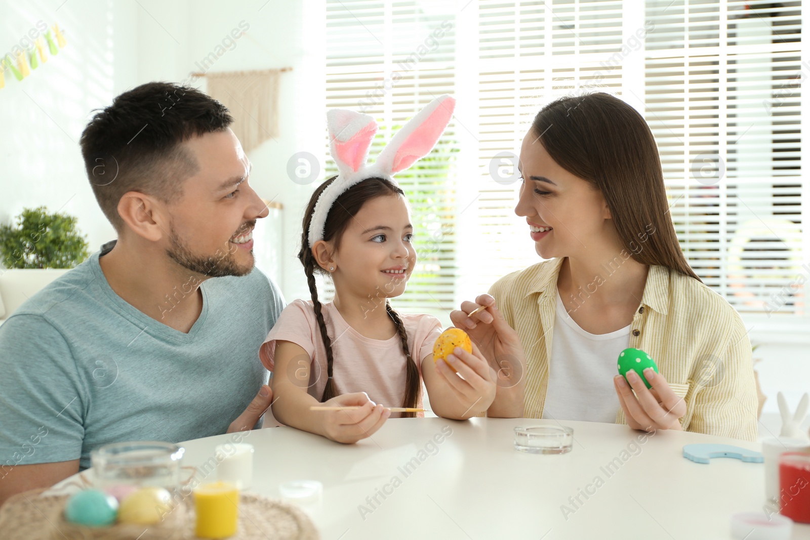 Photo of Happy father, mother and daughter painting Easter eggs at table indoors