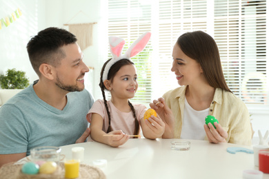 Happy father, mother and daughter painting Easter eggs at table indoors