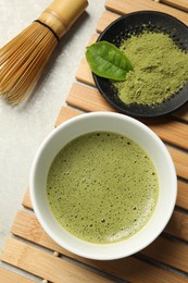 Photo of Cup of fresh matcha tea, green powder and bamboo whisk on table, flat lay