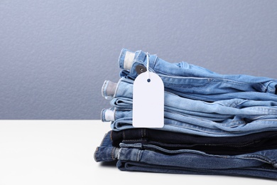 Photo of Stack of stylish jeans with tag on table