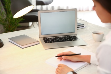 Photo of Woman working with modern laptop at white table, closeup. space for design